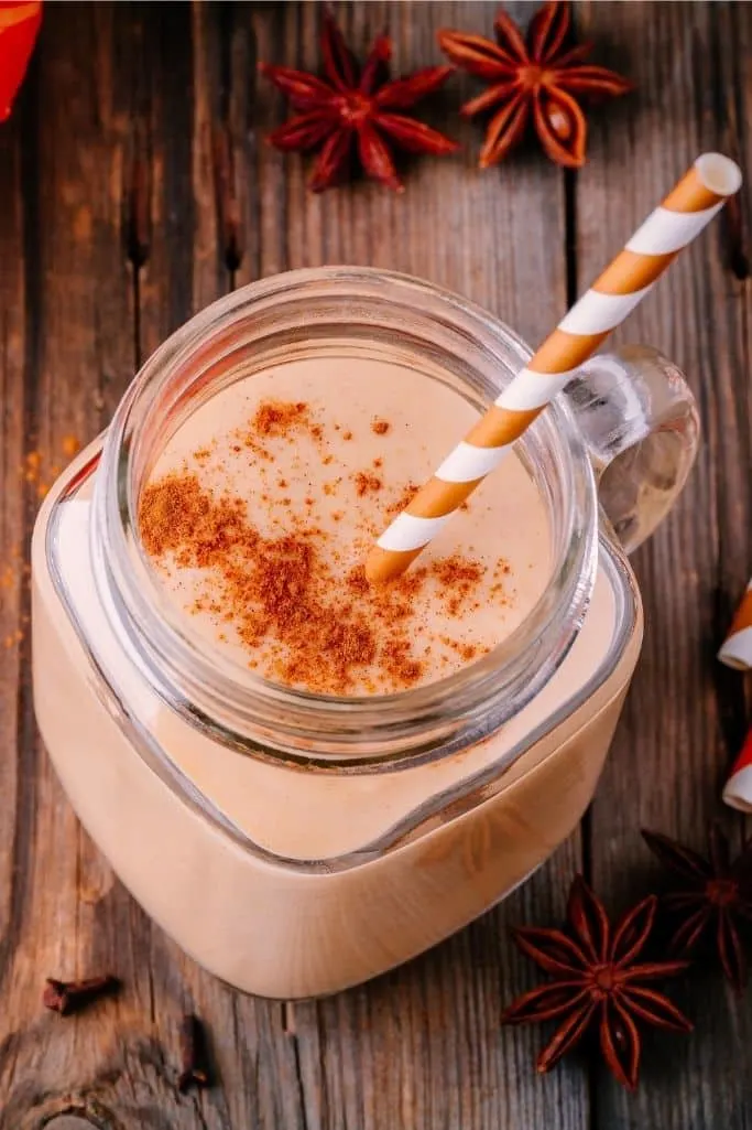 close up of pumpkin pie smoothie in glass with wood background