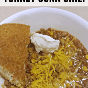 turkey corn chili in a white bowl with cornbread and sour cream and cheddar cheese