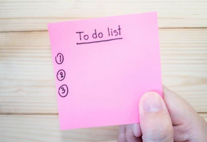 hand holding a pink sticky-note to-do list - the sticky note method makes managing your to-do list easier