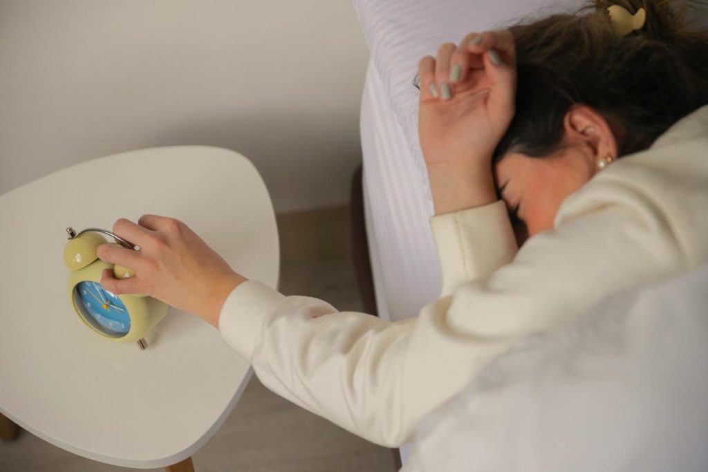 woman in bed reaching for alarm clock to turn it off