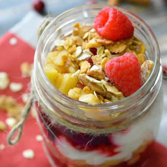 cranberry apple parfait in glass jar with granola and raspberries on top