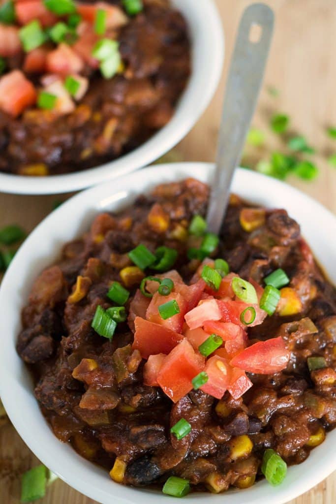 vegan chili in white bowls on a wooden cutting board