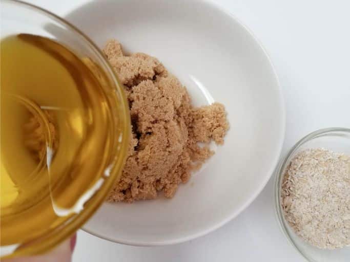 pouring olive oil into a white bowl containing brown sugar