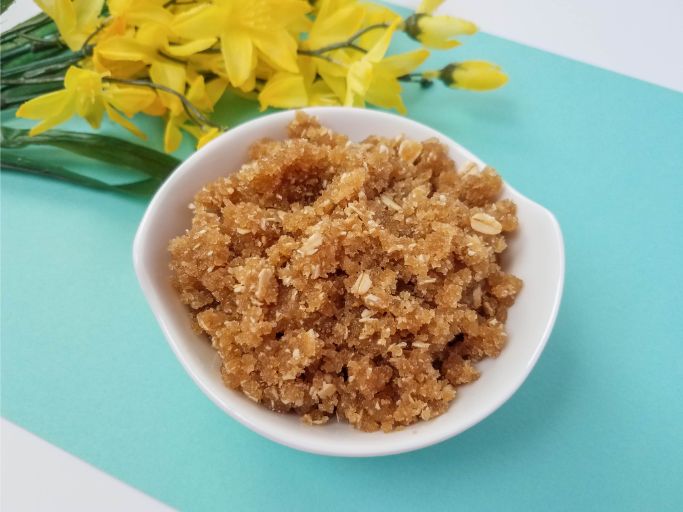natural homemade body scrub in a small white bowl with yellow flowers in the upper left corner