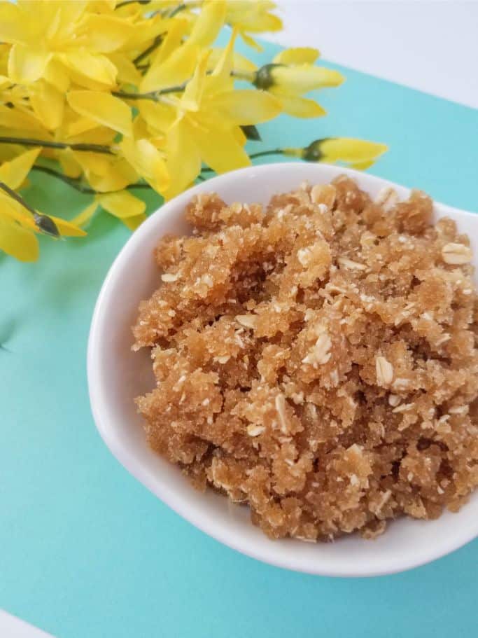 oatmeal brown sugar body scrub in a small white bowl with yellow flowers in the upper left corner