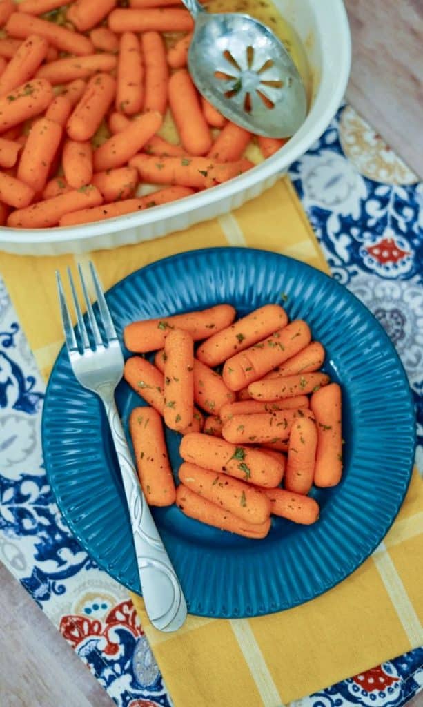 baby carrots roasted in the oven served on a blue plate with baking dish in upper left corner