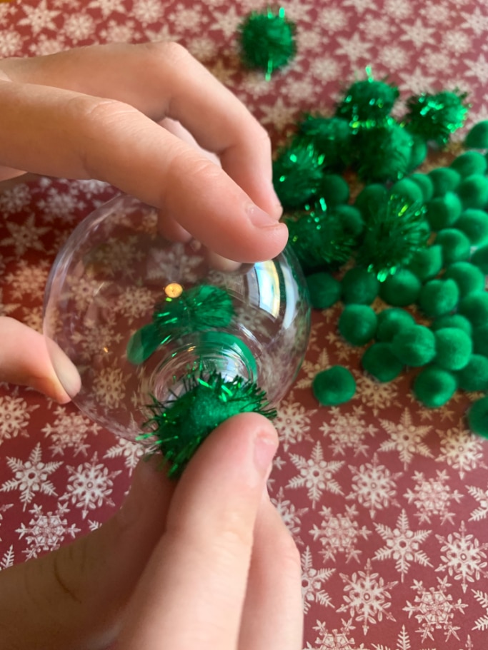 filling the clear ornament with green pom poms