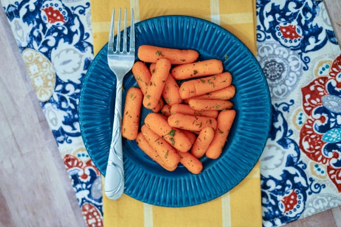 oven roasted baby carrots on a blue plate with serving fork