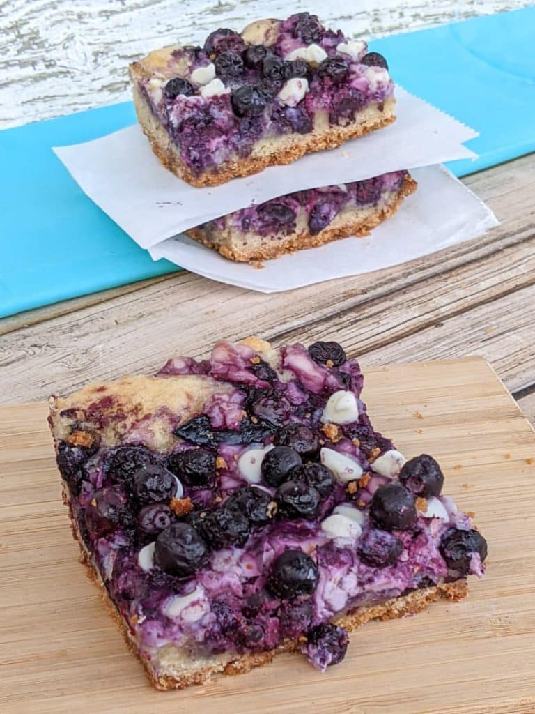 three blueberry bars with one on cutting board in foreground and two stacked in background