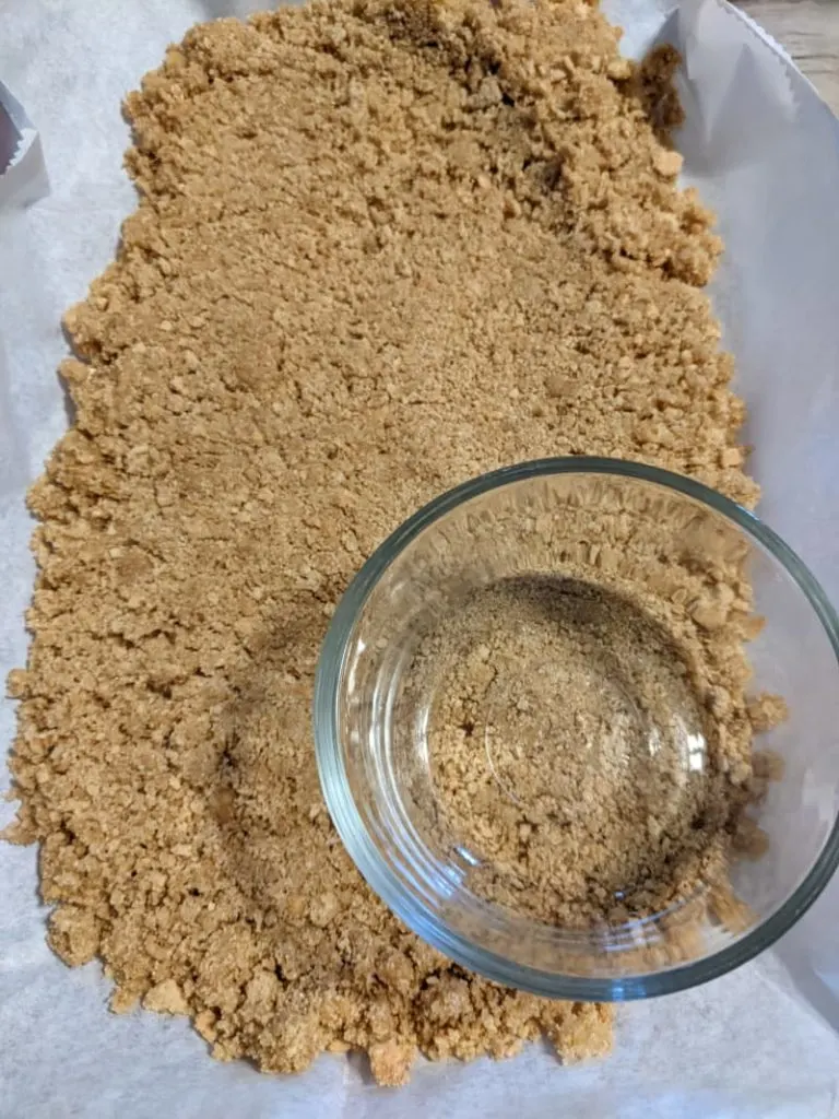 using a glass to press the graham cracker crust