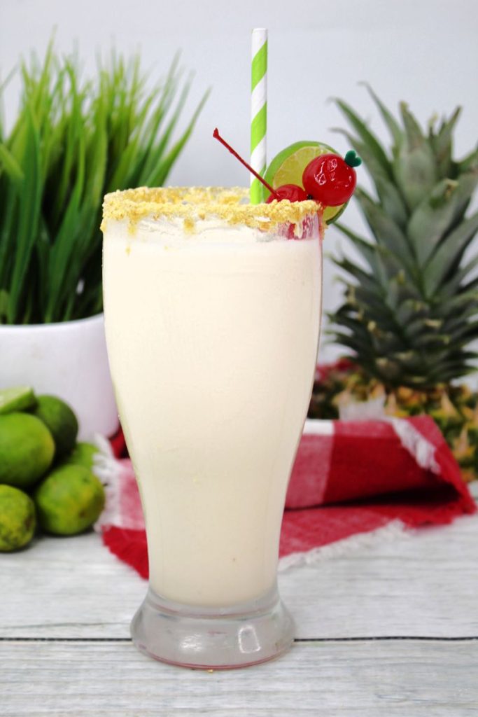 key lime colada in clear glass with graham cracker crumb rim and cherry and lime garnish