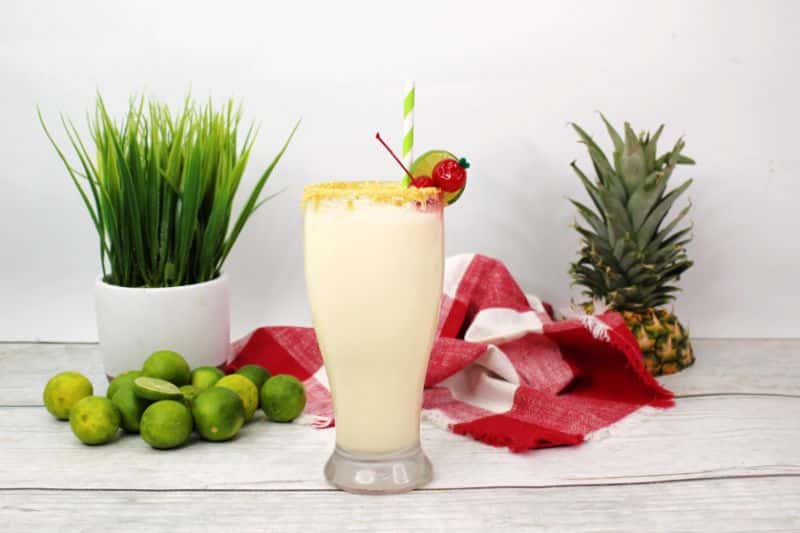 key lime pina colada on white background with limes, pineapple leaves, and checkered napkin