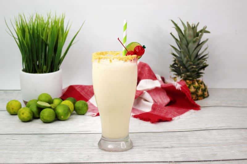 a sweet and tart key lime colada in a tall glass with tropical elements in background