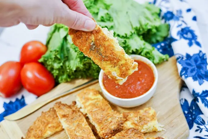 holding up one of the keto cheese sticks to dip in marinara sauce