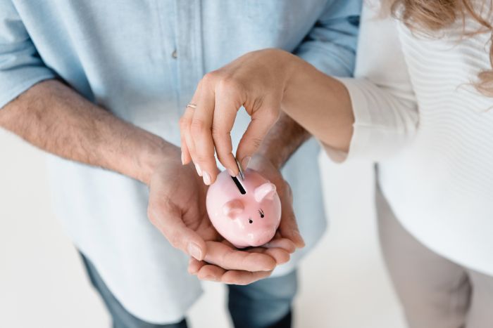 man's hands holding piggy bank with woman putting money in