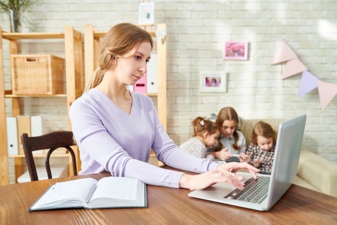 mom working on laptop at table with kids in background