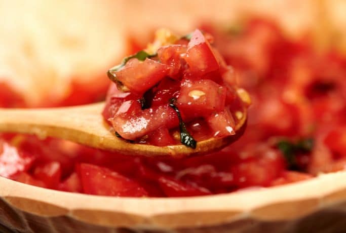 up close picture of diced tomatoes on wooden spoon
