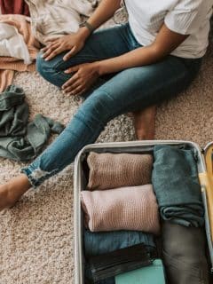 woman sitting on floor putting clothes in suitcase