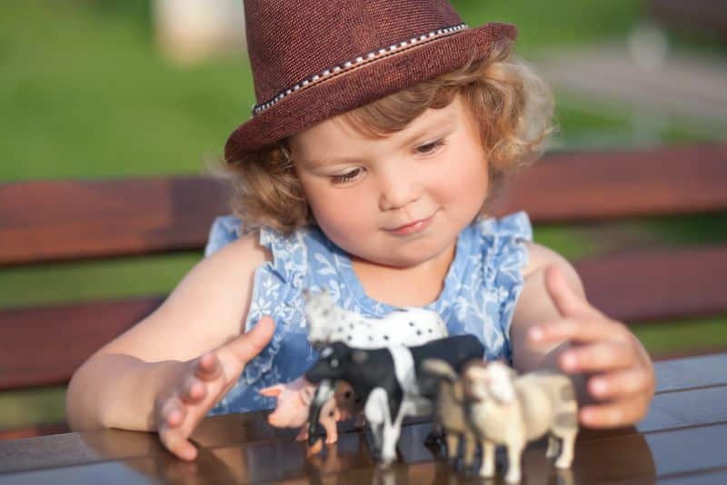girl in hat playing with farm animal toys