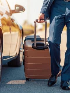 man in blue slacks pulling hard-case luggage