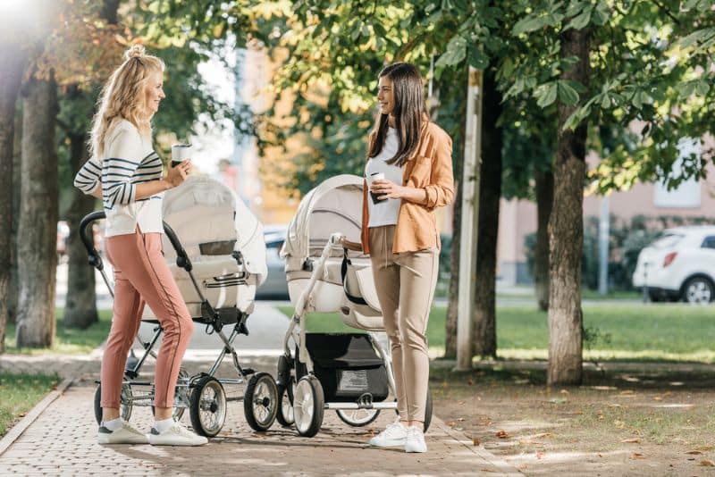 two moms holding coffee and pushing prams