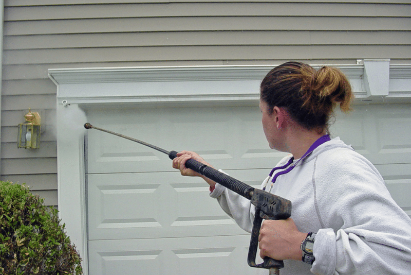 woman powerwashing garage door - home maintenance tips for exterior