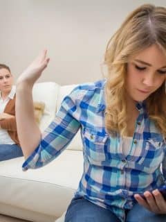teen girl with smartphone with frustrated mother in background