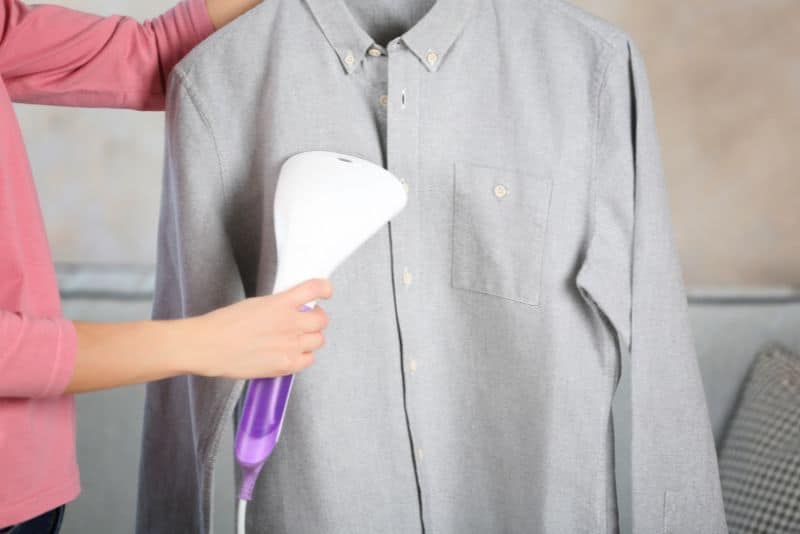 woman using portable steamer on gray shirt