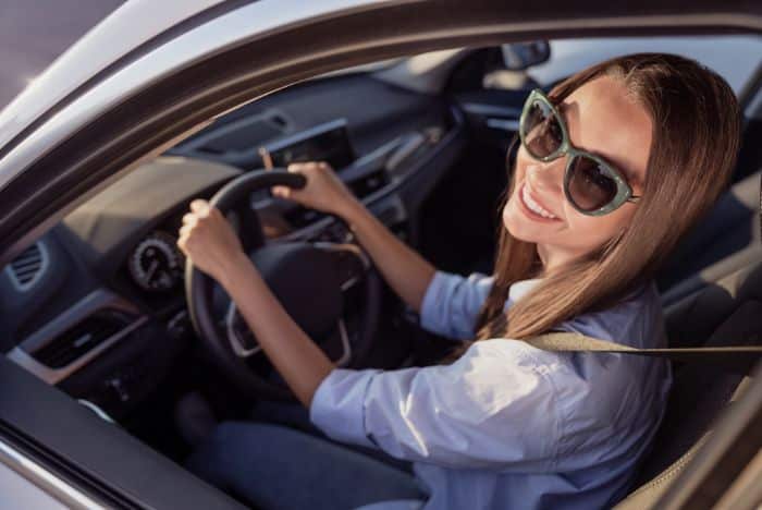 brunette in car wearing sunglasses with hands on steering wheel