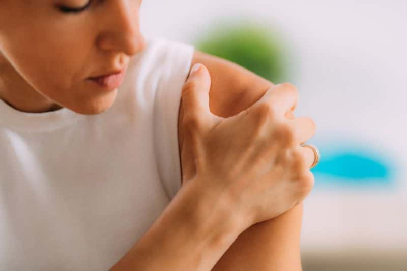 woman in white tank top rubbing shoulder