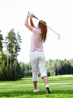 woman in pink shirt swinging a golf club