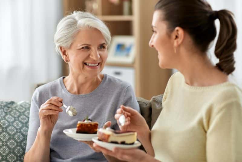 woman talking to elderly mother and eating cheesecake together
