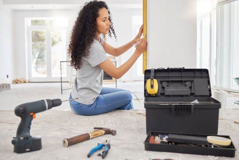 woman using a level and surrounded by tools for remodeling
