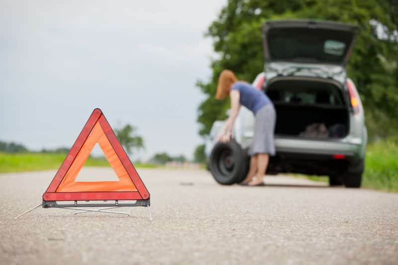 woman getting spare tire out of trunk of car