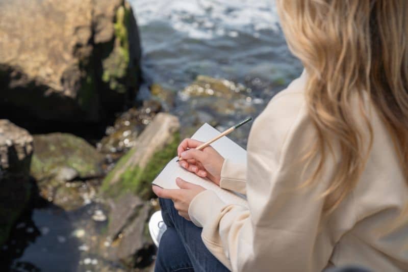 woman sitting by water writing in journal
