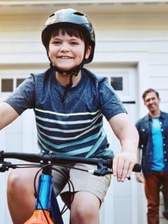 boy riding bicycle with father looking on smiling