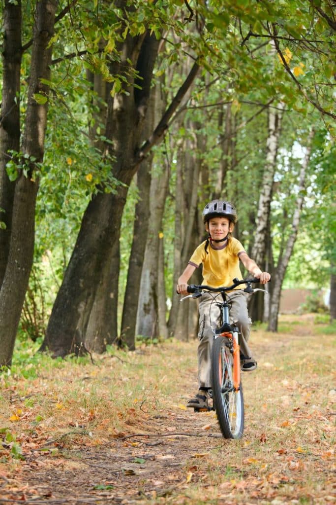 boy on bicycle wearing a helmet, forested area, riding toward camera