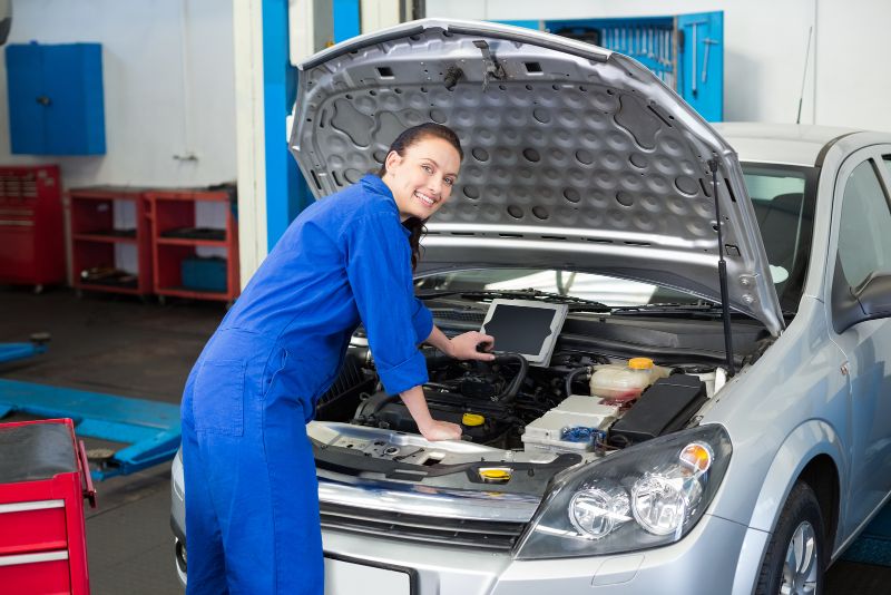 female mechanic looking over a car's engine
