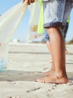 child barefoot on beach cleaning up