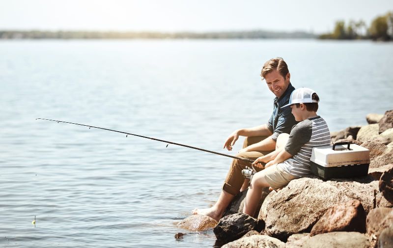 father fishing with son on rocky bank