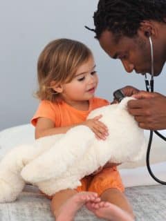 child with teddy bear being examined by doctor