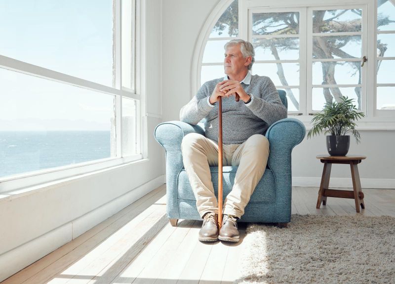 elderly man with cane sitting in armchair near window