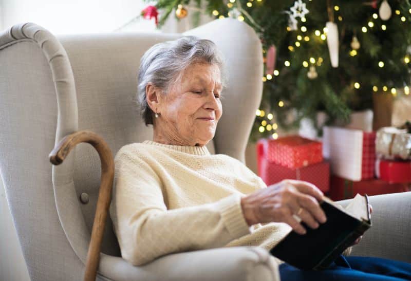 elderly woman reading and sitting in armchair by a Christmas tree 