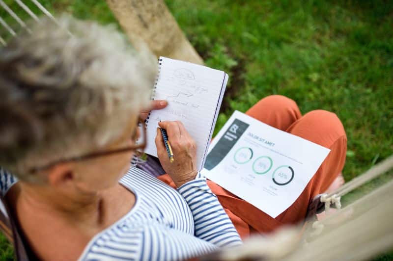elderly woman sitting outdoors making notes in a notebook
