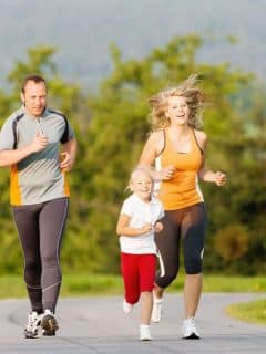 dad, mom, and daughter running together on paved road