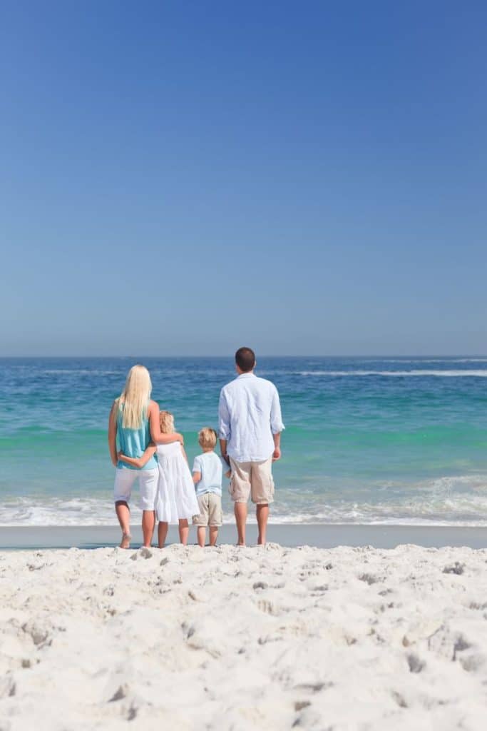 family of 4 standing on beach facing the ocean