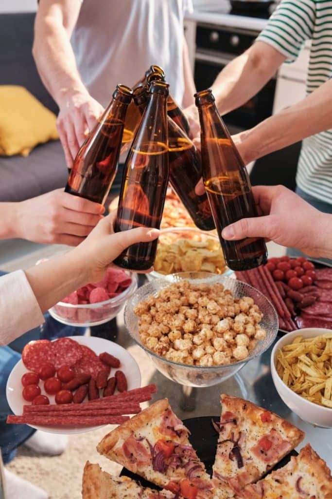 group clinking beer bottles together over food