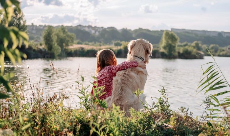 girl sitting with her dog by the water