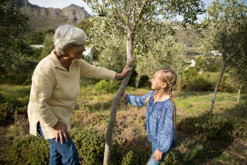 grandma and granddaughter smiling at each other standing at small tree