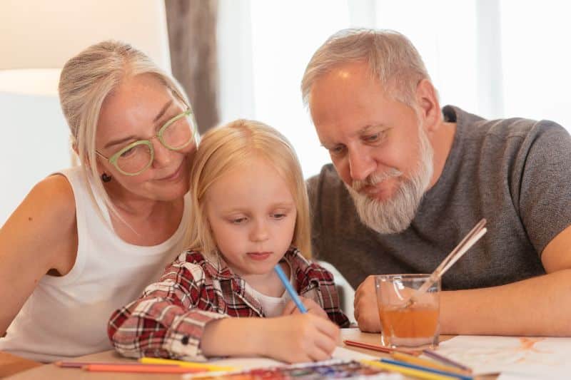 grandparents watching granddaughter paint on paper